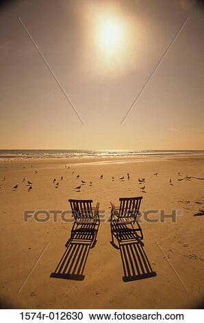 Stock Image - Rear view of two chairs on the beach at sunset. Fotosearch