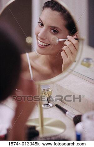 Stock Image - Reflection of a young woman applying blush with a make-up brush. Fotosearch