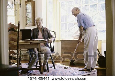 Senior man standing and holding a golf club with a senior woman using a laptop View Large Photo Image Stock Image - Senior man standing and holding a golf club with a senior woman using a laptop. Fotosearch