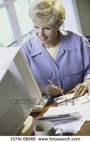 Stock Photograph - Senior woman sitting in front of a computer monitor. Fotosearch