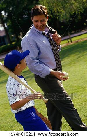 Stock Image - Side profile of a father walking in a park with his son carrying a baseball bat. Fotosearch