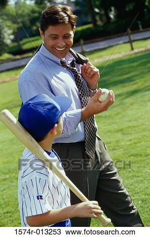 Stock Image - Side profile of a father walking in a park with his son carrying a baseball bat. Fotosearch