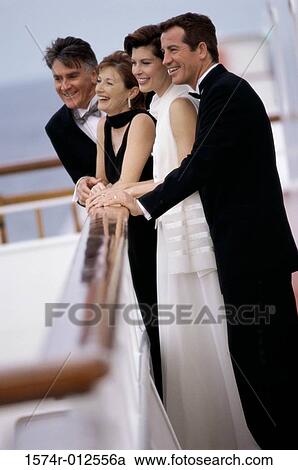 Stock Image - Side profile of a mid adult couple and a mature couple standing on the deck of a cruise ship laughing. Fotosearch