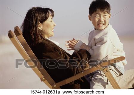 Stock Image - Side profile of a mother and son sitting in a beach chair. Fotosearch