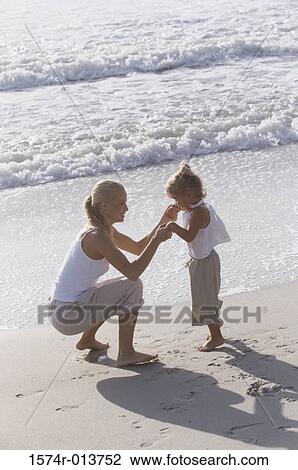 Stock Image - Side profile of a mother holding her daughter's hands on the beach. Fotosearch