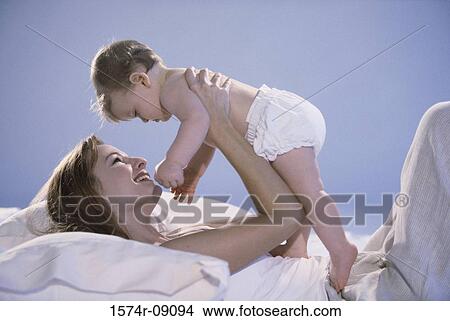 Picture - Side profile of a mother lying in bed holding her baby boy. Fotosearch