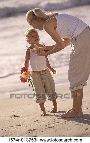Stock Image - Side profile of a mother showing a starfish to her daughter on the beach. Fotosearch