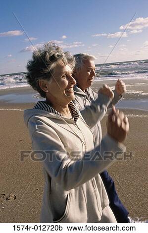 Stock Image - Side profile of a senior couple walking together on the beach. Fotosearch
