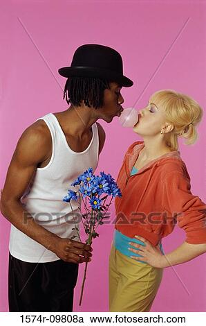 Stock Image - Side profile of a young couple blowing bubble gum. Fotosearch