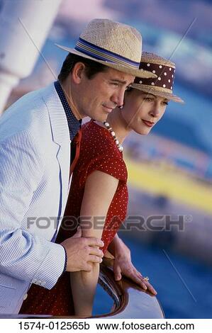 Stock Image - Side profile of a young couple standing on a cruise ship. Fotosearch