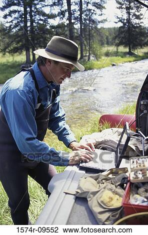 Stock Image - Side profile of a young man standing outdoors using a laptop. Fotosearch