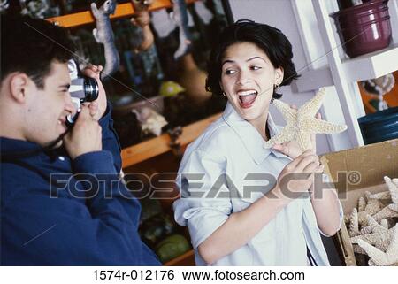 Stock Photograph - Side profile of a young man photographing a young woman holding a starfish. Fotosearch