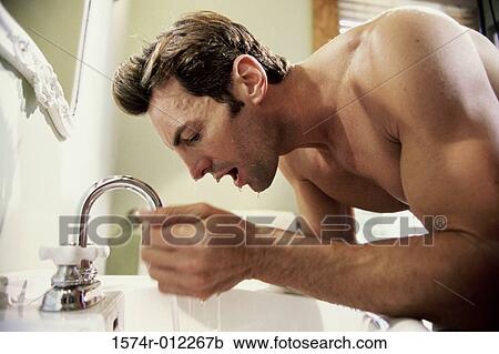 Stock Image - Side profile of a young man washing his face. Fotosearch