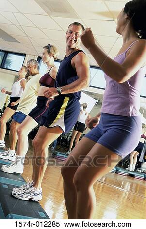 Stock Photography - Side profile of five people doing step aerobics in a gym. Fotosearch