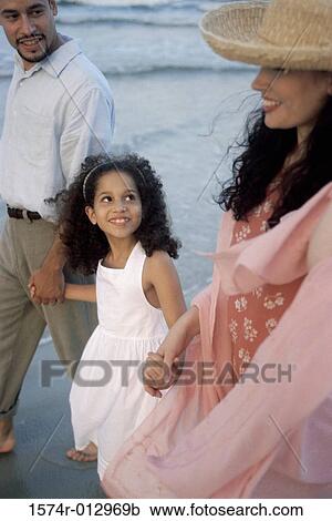Stock Image - Side profile of parents and their daughter walking on the beach. Fotosearch