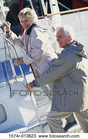 Stock Image - Side profile of senior couple stepping on a boat. Fotosearch