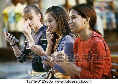 Stock Image - Side profile of three teenage girls grooming themselves. Fotosearch