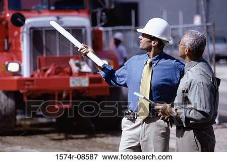 Side profile of two foremen discussing at a construction site View Large Photo Image Stock Photo - Side profile of two foremen discussing at a construction site. Fotosearch
