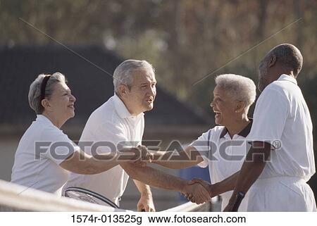Stock Image - Side profile of two senior couples shaking hands on a tennis court. Fotosearch
