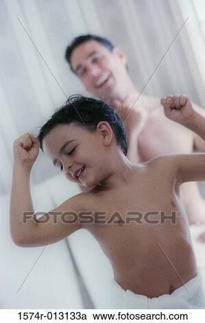 Stock Image - Son flexing his muscles with his father standing behind him. Fotosearch