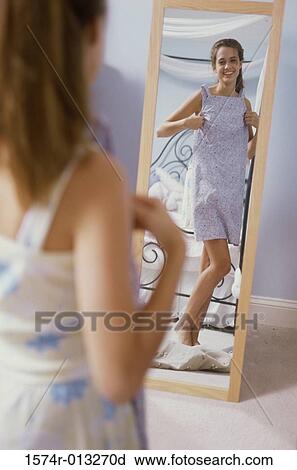 Stock Image - Teenage girl trying on a new dress in front of a mirror. Fotosearch