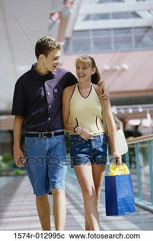Stock Image - Teenage girl walking with a young man carrying a shopping bag. Fotosearch