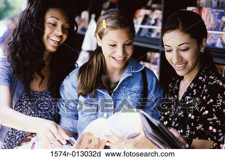 Stock Image - Three teenage girls reading a magazine. Fotosearch