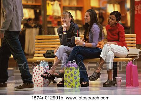 Stock Image - Three teenage girls sitting on a bench. Fotosearch
