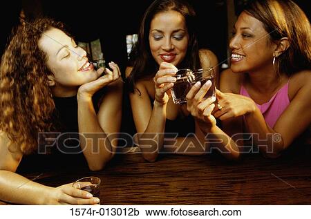 Stock Image - Three young women toasting with glasses in a bar. Fotosearch