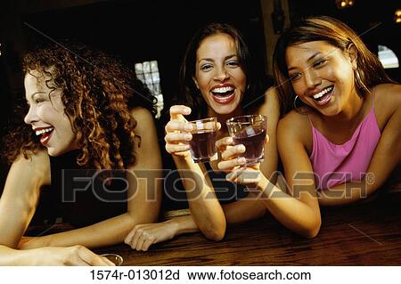 Stock Image - Three young women toasting with glasses in a bar. Fotosearch