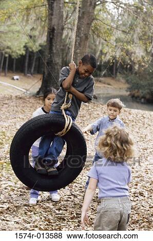 Two boys and two girls playing on a tire swing View Large Photo Image Stock Photo - Two boys and two girls playing on a tire swing. Fotosearch