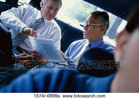 Stock Image - Two businessmen sitting in a car looking at documents. Fotosearch