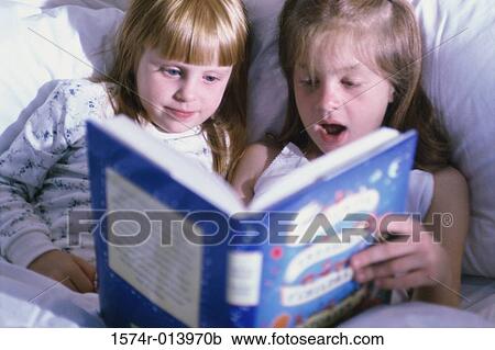 Stock Image - Two girls reading a book in bed. Fotosearch