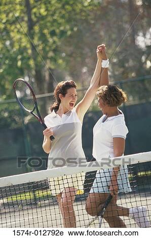 Stock Image - Two mid adult women cheering after winning a tennis match. Fotosearch