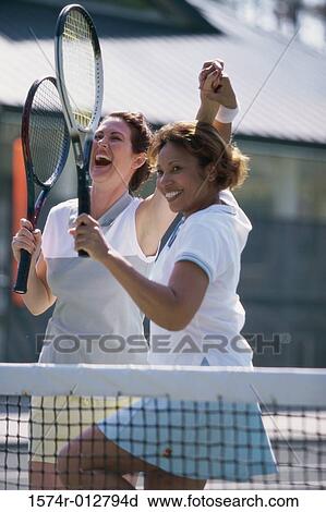 Stock Image - Two mid adult women cheering after winning a tennis match. Fotosearch