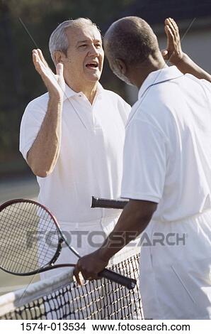 Picture - Two senior men giving high-five to each other on a tennis court. Fotosearch