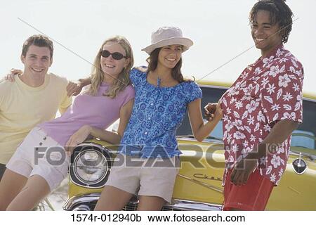 Stock Image - Two teenage couples leaning against a car. Fotosearch