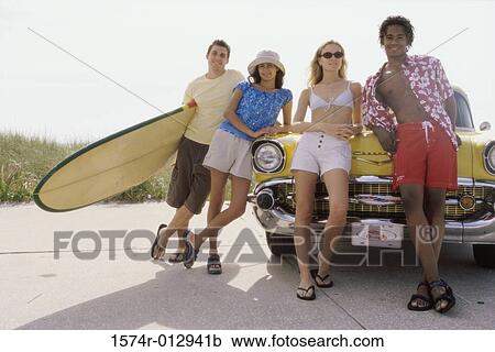 Stock Image - Two teenage couples leaning against a car. Fotosearch