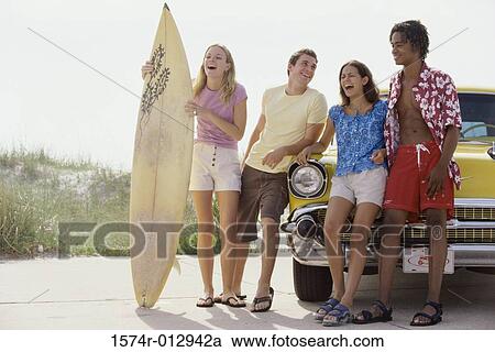 Stock Image - Two teenage couples leaning against a car. Fotosearch