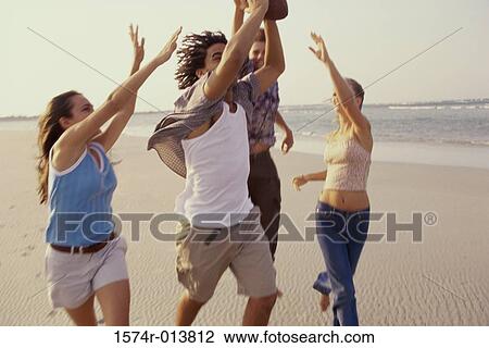 Stock Image - Two teenage couples playing football on the beach. Fotosearch