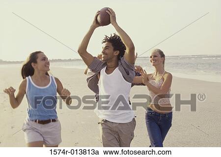 Stock Image - Two teenage couples playing football on the beach. Fotosearch