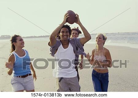 Stock Image - Two teenage couples playing with a football on the beach. Fotosearch