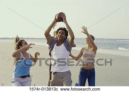 Stock Image - Two teenage couples playing with a football on the beach. Fotosearch
