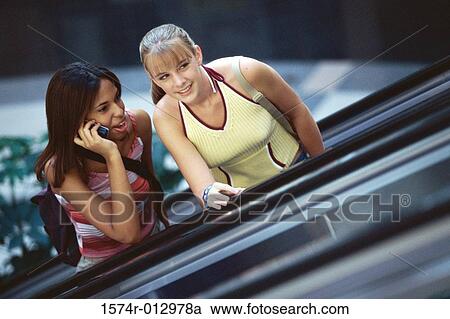 Stock Image - Two teenage girls standing on an escalator. Fotosearch