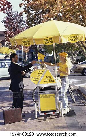 Stock Photo - Woman selling a hot dog to a businessman on the sidewalk. Fotosearch