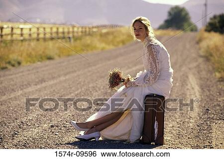 Young bride sitting on a suitcase at the side of a road View Large Photo Image Stock Photograph - Young bride sitting on a suitcase at the side of a road. Fotosearch