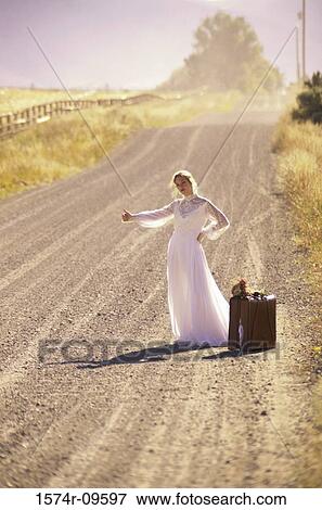 Stock Photo - Young bride standing at the side of a road with a suitcase. Fotosearch