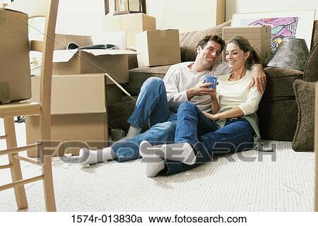 Stock Image - Young couple holding a coffee cup sitting on the floor. Fotosearch