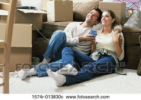 Stock Image - Young couple holding a cup of coffee sitting on the floor. Fotosearch