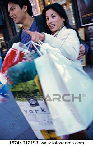 Young couple holding shopping bags walking in a market View Large Photo Image Stock Image - Young couple holding shopping bags walking in a market. Fotosearch
